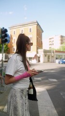 Wall Mural - A delightful young brunette stands on the street, holding a smartphone.