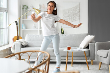 Wall Mural - Young woman in headphones dancing on her day off at home