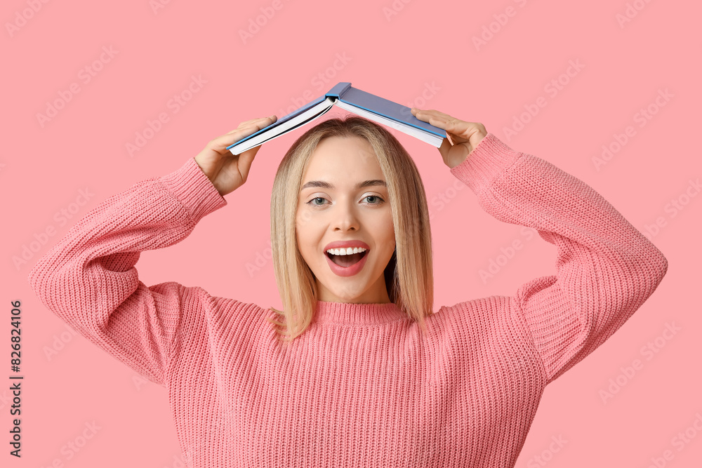 Beautiful happy young woman with book on pink background