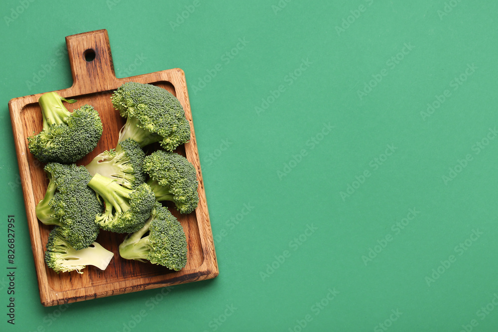 Wooden board with fresh broccoli cabbages on green background
