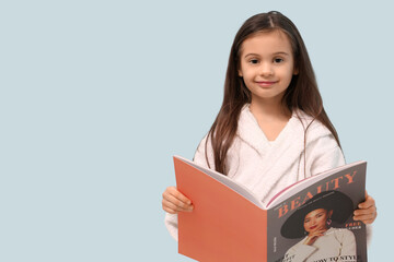 Wall Mural - Cute little happy girl in bathrobe reading magazine on blue background