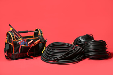 Tool bag, rolled flexible conduit tube and cables on red background