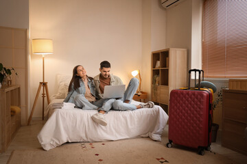 Poster - Young couple of tourists using laptop in hotel room at night