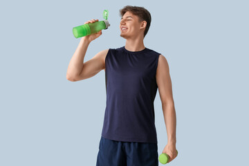 Wall Mural - Sporty young man with bottle of water and dumbbell on light background