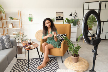 Wall Mural - Young African-American witch with rune in armchair recording video at home