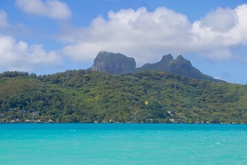 Wall Mural - Bora Bora's extinct volcano rises above the pastel-huedwaters of the surrounding lagoon