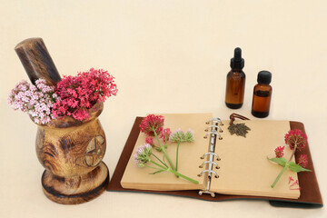 Wall Mural - Red and pink valerian herb flowers in a mortar with old hemp notebook and essential oil bottles. Used in traditional perfume making. On hemp paper background. Valeriana.