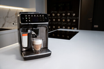 Modern automatic coffee machine makes latte in double wall glass on a table