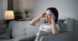 © Johnstocker - Portrait of Unwell young woman have a high fever and massaging temples to relieve headache while sitting on sofa in the living room at home, healthcare woes