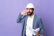 © luismolinero - Young architect man with helmet and holding blueprints over isolated purple background listening to something by putting hand on the ear