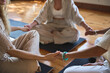 © insta_photos - Three diverse women group sitting in circle meditating together doing exercises giving support at body care training. Yoga coach holding hands of women group during holistic healing session. Close up.