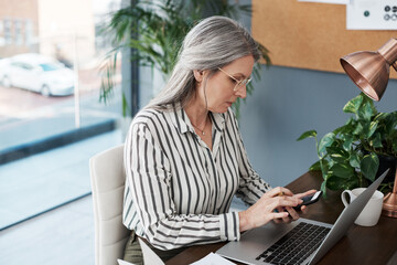 Leinwandbilder - Phone, laptop and mature business woman reading email, networking and scroll on app in startup. Smartphone, computer and manager research information on website for creative work project of editor