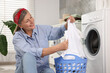 © New Africa - Happy housewife with laundry basket near washing machine at home