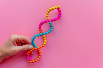 Poster - Hand holding a vibrant beaded DNA strand against a pink background, symbolizing the creativity and uniqueness in genetic research