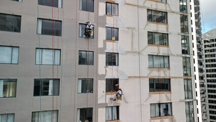 This captivating drone photo shows skilled workers performing maintenance tasks on a scaffold at a considerable height. The precision and risk involved in urban repair are evident in their actions.