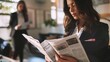 © Bijac - businesswoman reading newspaper while conversing with colleague professional workplace scene