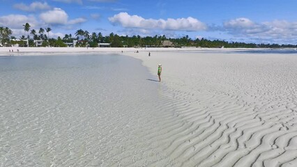 Wall Mural - Aerial view of alone young woman on the sandbank in ocean, white sand, blue sea during low tide at sunny summer day in Zanzibar island. Top view of girl, sand spit, bay, clear water, sky with clouds