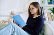 © Valerii Honcharuk - Young woman reading book, sitting on couch at home, engrossed in fiction
