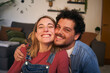 © CarlosBarquero - Portrait two cheerful young in love looking at smiling camera sitting in living room. Caucasian couple in affectionate attitude hugging at home. Happy romantic relationship people making life together