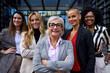 © CarlosBarquero - Portrait group formal business women of different ages looking smiling at camera together with happy expression outdoors. Mature Caucasian professional female leader posing arms crossed in foreground