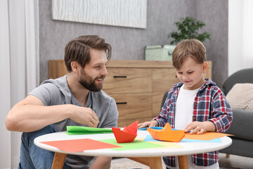 Canvas Print - Dad and son making paper boats at coffee table indoors