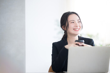 Wall Mural - woman looking up holding coffee and using computer in office Bright image of job change, hiring, etc. Copy space on the right