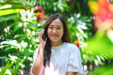 Wall Mural - Portrait image of a young woman holding and talking on mobile phone in the garden