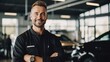 © Photolife   - smiling caucasian car dealership technician in uniform looking at camera against background of cars in service center