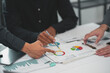 ©  NCST Studio - Business meeting with professionals analyzing graphs and charts on paper, discussing financial data and development strategies.