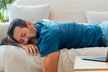 One man fall asleep at home for afternoon nap laying on the sofa with open laptop on the table. Tired people sleep during the daylight. Overwork stress concept lifestyle health. Sleeping on couch