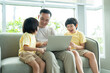 © Supachai - Asian father and his two sons have fun watching video in laptop while sitting on sofa in living room at home. Family relaxing on holiday.