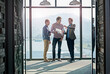© peopleimages.com - Business people, men and partnership with paperwork for planning by window of office for b2b brainstorming. Collaboration, employees and ideas with document for financial review and project report