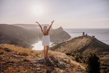 Wall Mural - A woman is standing on a hill overlooking a body of water. She is wearing a white dress and she is happy.