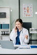 © Nuttapong punna - Young female doctor in white medical uniform using laptop and tablet talking video conference call at desk,Doctor sitting at desk