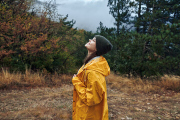 Wall Mural - A woman wearing a yellow raincoat standing in the middle of a lush field surrounded by trees and nature