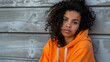© Michael - Contemplative young woman in an orange hoodie poses against a gray wooden backdrop