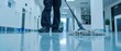 © ARTIFICIAN - a janitor diligently mops an office floor, with the mop in close-up focus. The cleaner works tirelessly to ensure the floors are spotless and gleaming