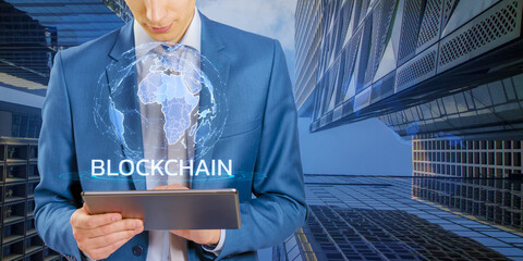 Aufkleber - A man in a blue suit holding a tablet with a blockchain concept graphic, standing against a modern building background