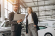 © anatoliycherkas - A male salesman showing something on a laptop to a female client buying a car inside a car dealership