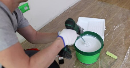 Wall Mural - Builder mixes paint in bucket with mixer on floor. Preparing paint for wall painting