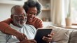 © LukaszDesign - Senior couple uses iPad to video contact family and friends on sofa at home. Happy elderly grandparents Enjoy retirement by laughing and smiling.