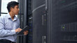 © Pixza - A technician in a blue shirt uses a tablet while inspecting a server rack in a modern data center, ensuring proper functionality.