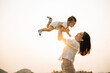 © sorapop - In a carefree summer moment, mom holds her cute toddler son up high, throwing him up into sky. playful child enjoys freedom of flying, while cheerful mother smiles and enjoy moment of family happiness