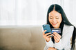 © sorapop - Smiling woman with smartphone and credit card shops online on sofa. Engaged in ordering banking and buying goods or services. Modern technology for convenient shopping at home.