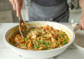 Woman cooking a delicious cream chicken pan dish with chicken breast, peas and carrots in a skillet 