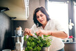 © Halfpoint - Beautiful mature woman taking care of herbs, cutting herbs for cooking in kitchen.