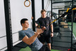 © dikushin - Professional fitness trainer showing sportsman how to train with trx fitness straps in gym. Sporty fit male instructor showing suspension training to motivated man, performing pull-ups exercise.