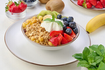 Wall Mural - Granola with strawberries, kiwi, banana and blueberries in a round plate on a white table.