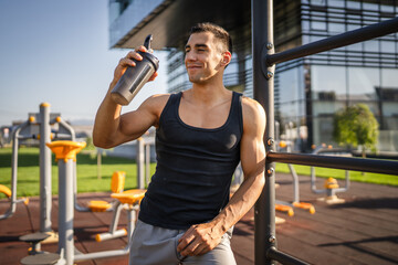 Poster - One caucasian man young male athlete take a brake during outdoor training in the park outdoor gym hold supplement shaker in hand happy confident strong copy space