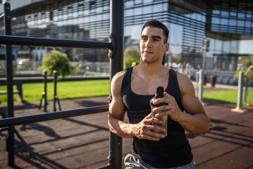 Canvas Print - One caucasian man young male athlete take a brake during outdoor training in the park outdoor gym hold supplement shaker in hand happy confident strong copy space